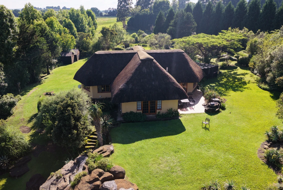 Thatched cottage in lush green landscape.